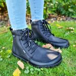 Black leather barefoot boots with laces, worn with light blue jeans on grass.