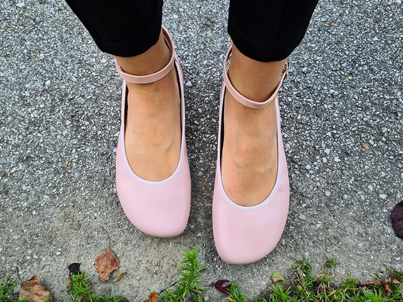 Top view of light pink Shapen Tulip barefoot flats with elastic trim, worn with black leggings on concrete.