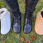 Three pairs of barefoot boots – white fur-lined, classic black lace-up, and tan Chelsea – side by side on grass.
