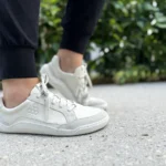 Light-colored barefoot sneakers worn outdoors on pavement