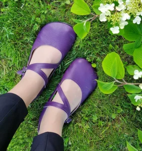 Purple barefoot ballet flats from Softstar Shoes with criss-cross ankle straps, worn on grass.