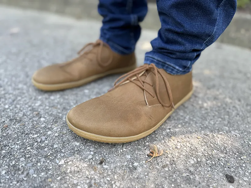 Side view of Vivobarefoot Ra IV barefoot shoes in brown leather, worn with jeans while standing on pavement