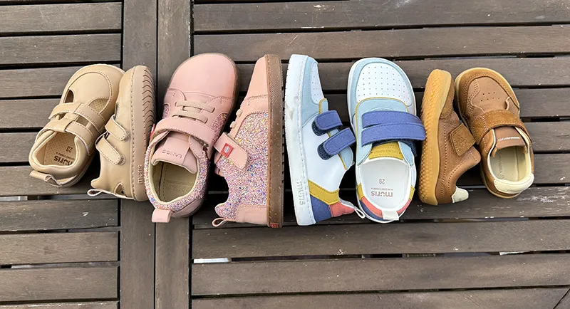 4 pairs of kids’ barefoot shoes in different colors and styles arranged in a row on a wooden surface