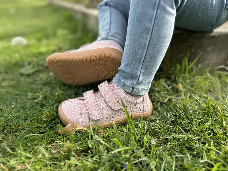 Child in pink barefoot shoes with velcro straps sitting on grass