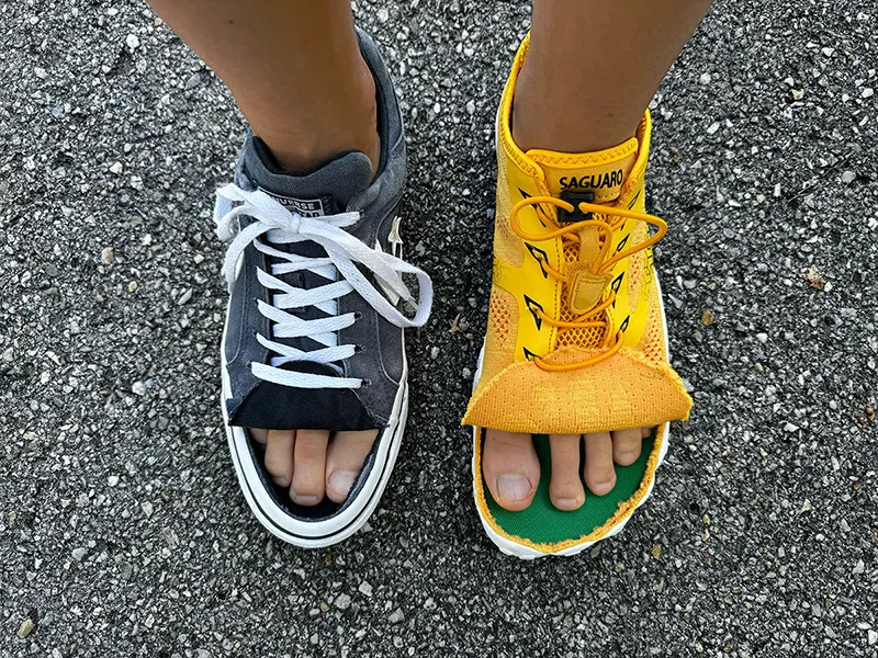 One foot wearing a cut Converse sneaker and the other a cut Saguaro barefoot shoe, showing how much more toe space barefoot shoes give
