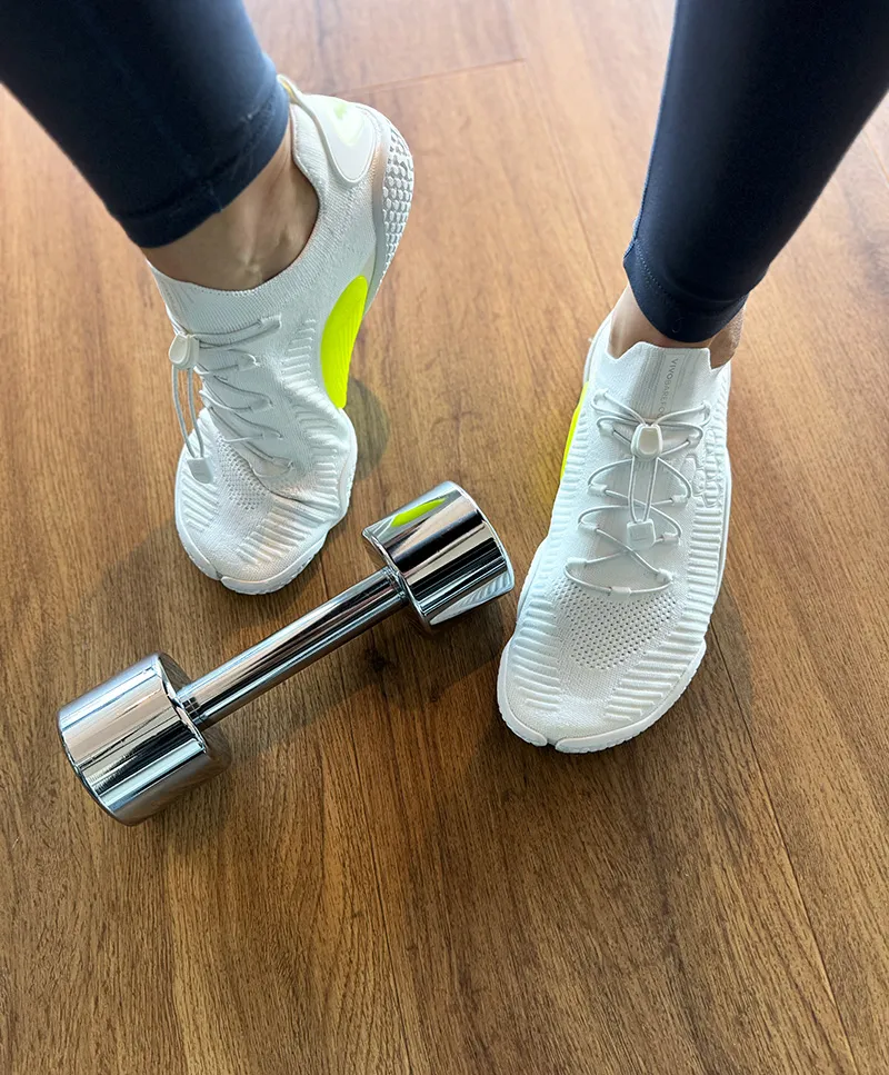 White barefoot training shoes worn in the gym next to a dumbbell.
