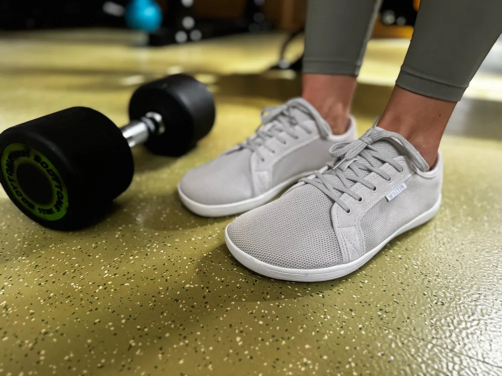 Minimalist barefoot sneakers for gym workouts shown beside weights.