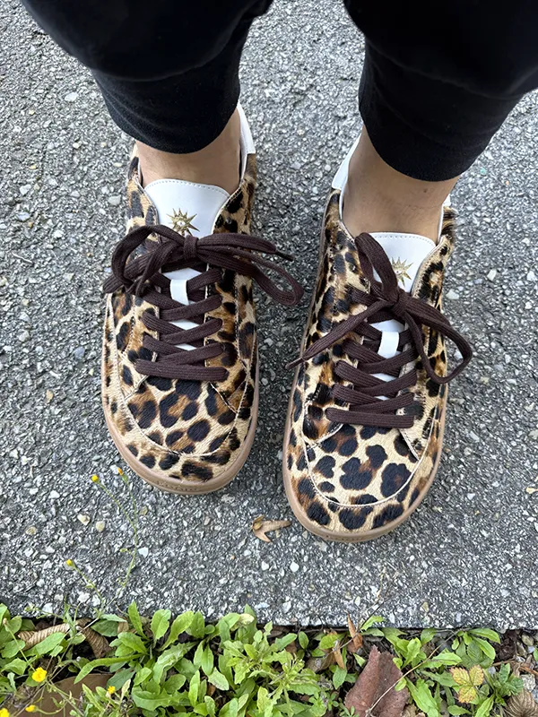 Leopard-print barefoot sneakers with wide toe box, worn with black leggings on pavement.