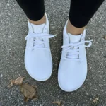 White barefoot sneakers with wide toe box, worn with black leggings on concrete ground.