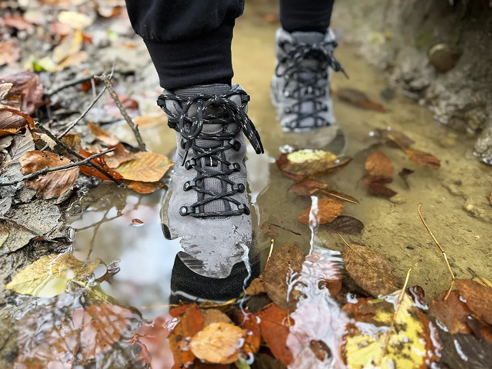 Black barefoot hiking boots standing in a shallow puddle with fallen leaves.