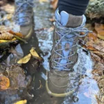 Blue barefoot winter boots standing in a puddle with fallen leaves.