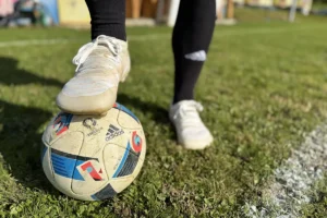 White barefoot soccer cleats stepping on the ball near the sideline.