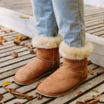 Tan suede barefoot winter boots with shearling trim photographed on a wooden walkway.