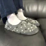 Dark gray barefoot slippers with dotted pattern worn on sofa.