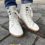 Light-colored barefoot lace-up boots worn with rolled jeans on a paved walkway.